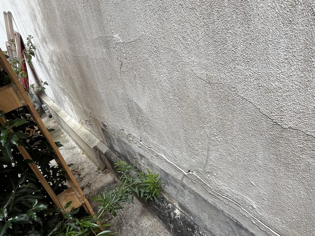 Fissures et dégradation d’un enduit sur la partie basse d’un mur ancien